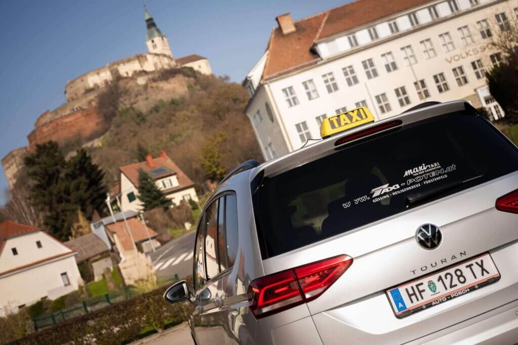 Taxi vor historischem Gebäude auf einem Hügel in malerischer Stadtlandschaft.